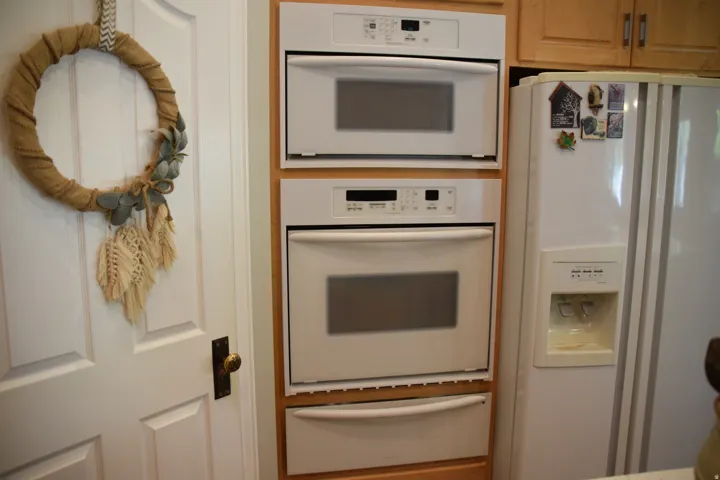 Built-in wall oven and microwave combination unit, white side-by-side refrigerator with ice and water dispenser, and light wood-finish cabinetry