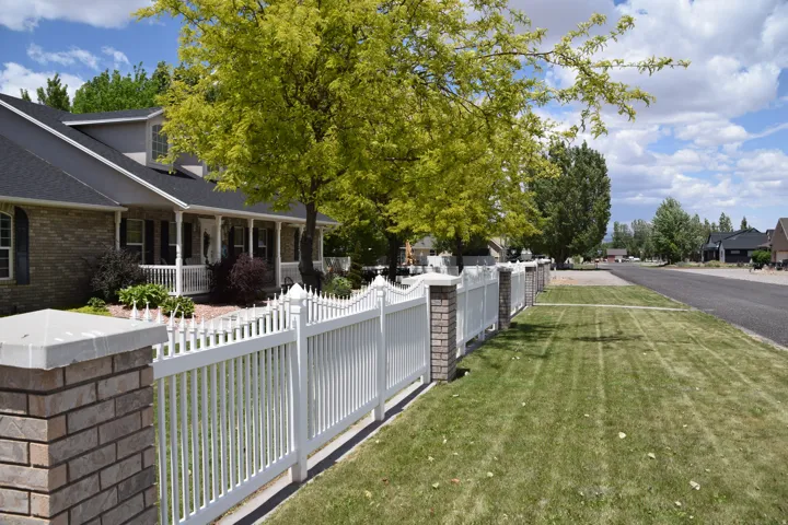Brick and vinyl picket fence framing a landscaped front yard with mature trees