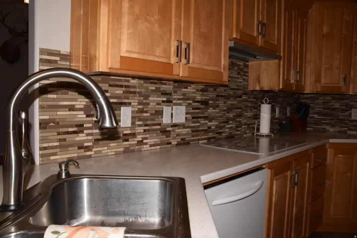 Stainless steel sink with a high-arch faucet, complemented by light wood cabinetry, a mosaic tile backsplash, and light-toned countertops