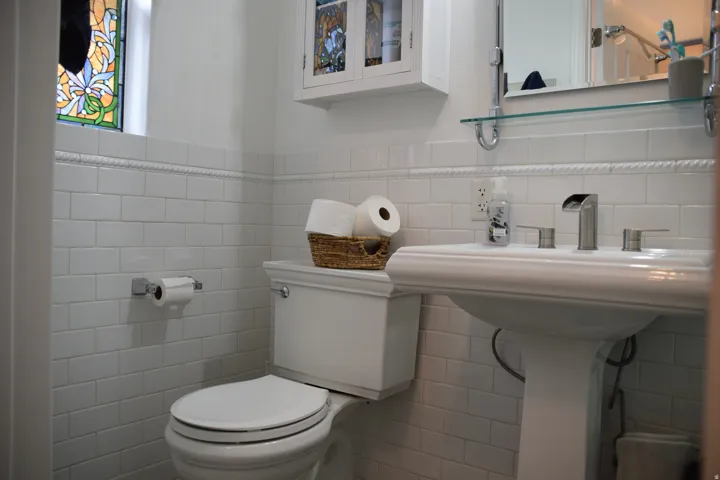 Bathroom featuring a pedestal sink, white subway tile wainscoting, and a stained glass window accent