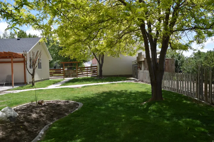 Expansive backyard featuring a manicured lawn, established trees, and a concrete paver pathway