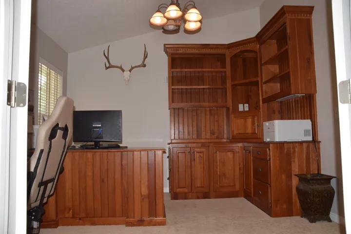 Room featuring custom wood-finish built-in cabinetry and shelving, a matching wood-finish desk, and vaulted ceilings