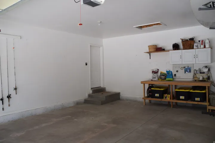 Spacious garage featuring a concrete floor, painted white walls, and a side entry door with concrete steps