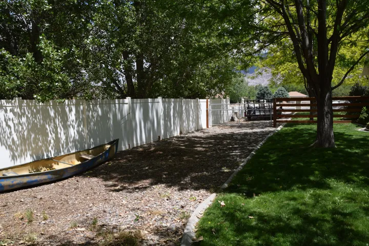 Expansive gravel-covered side yard featuring a white privacy fence and a dark wood fence