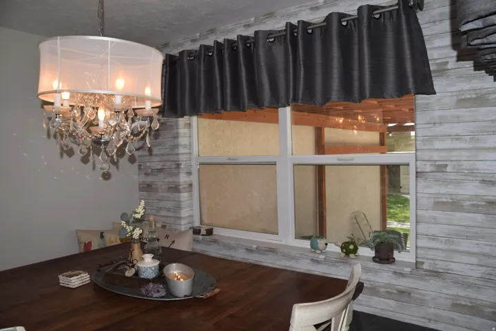 Dining area featuring an elaborate chandelier with a sheer drum shade and crystal accents, a window with a valance, and distressed wood-finish accent paneling