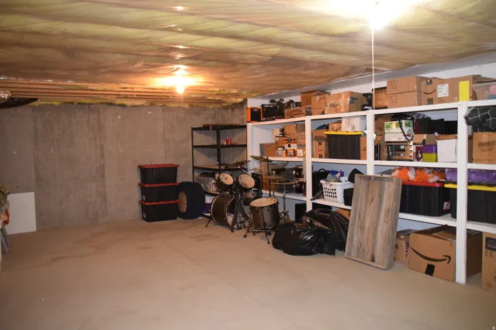 Unfinished lower level featuring concrete walls, exposed ceiling joists with insulation, concrete flooring, and built-in shelving units