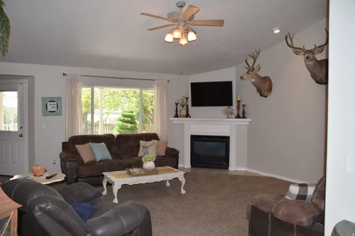 Living area featuring a white fireplace mantel, an electric fireplace insert, and a ceiling fan with integrated lighting