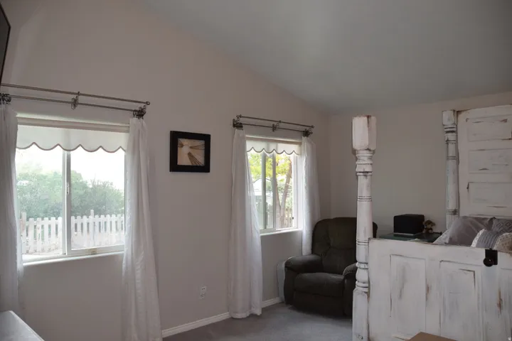 Vaulted ceiling bedroom featuring two windows with white window treatments, light gray walls, and gray carpet