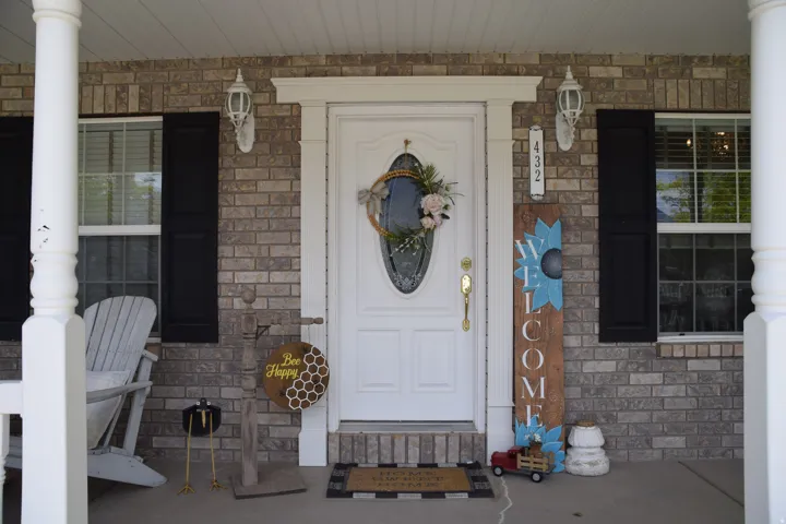 Brick facade featuring a white entry door with an oval glass insert, flanked by two windows with black louvered shutters