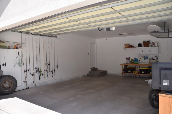 Spacious garage with concrete flooring, white painted walls, built-in shelving, and a workbench with storage