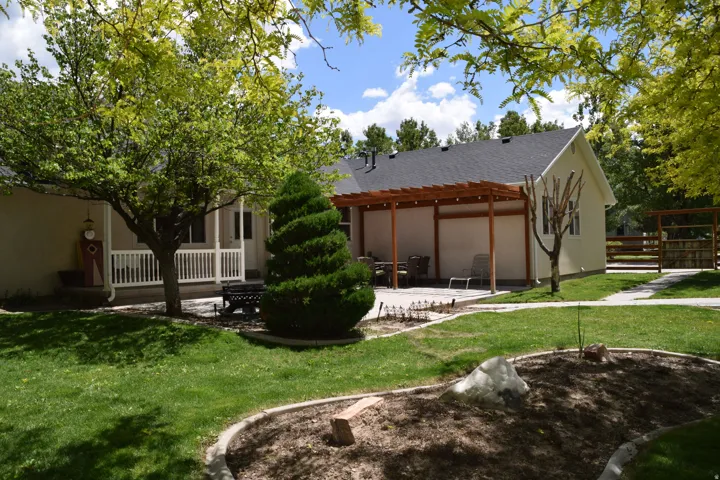 Spacious backyard featuring a wood pergola over a concrete patio, a covered porch with white railing, a manicured lawn, and mature trees