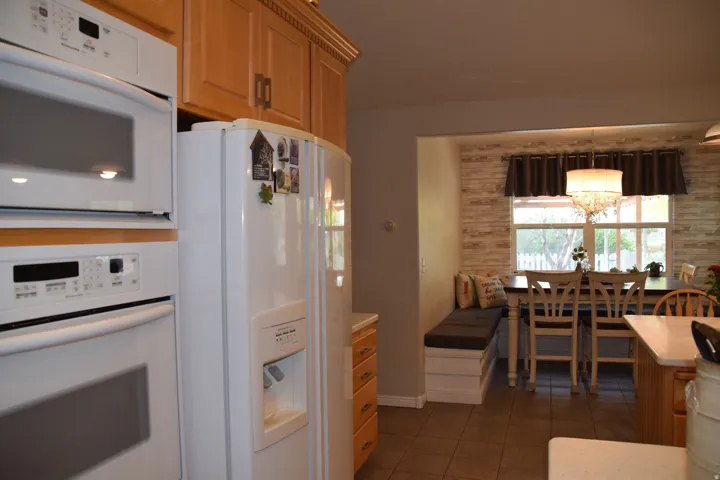 Kitchen featuring light wood cabinetry, integrated white appliances including a built-in microwave and oven, and a white refrigerator