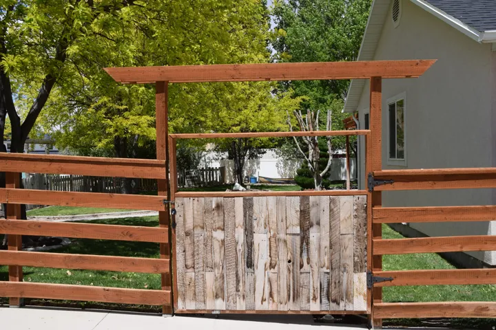 Wood fence with a contrasting wood-plank gate, featuring black hardware and an overhead pergola