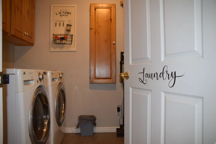 Dedicated laundry area featuring wood-finish cabinetry, a white panel door with brass-tone hardware, light neutral wall paint, and tile flooring