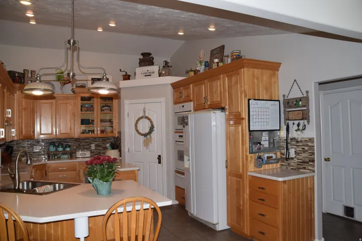 Spacious kitchen featuring warm wood cabinetry, a central island with integrated sink, recessed lighting, a stone tile backsplash, and built-in appliances