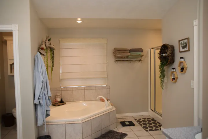 Corner soaking tub with tile surround, separate shower with glass enclosure, recessed ceiling lighting, and neutral wall tones