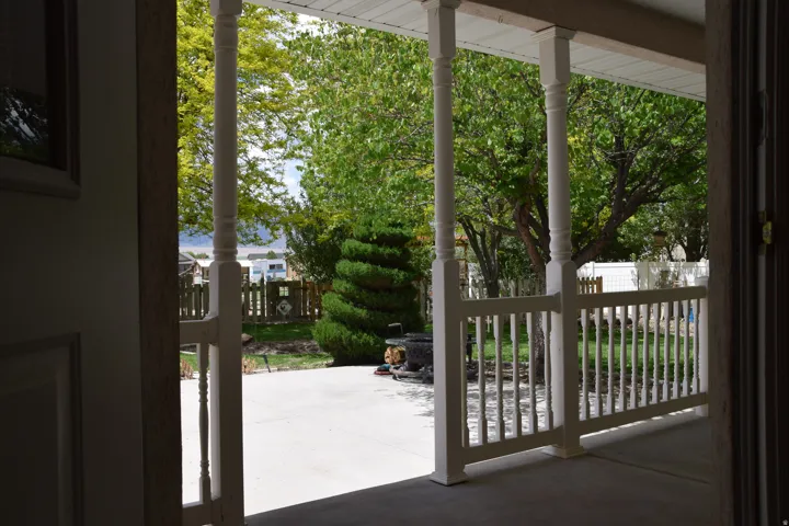 Covered porch featuring white columns and balusters, with a concrete patio surface