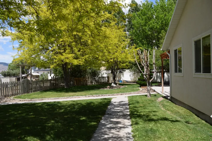 Spacious side yard featuring mature trees, a manicured lawn, and a concrete pathway