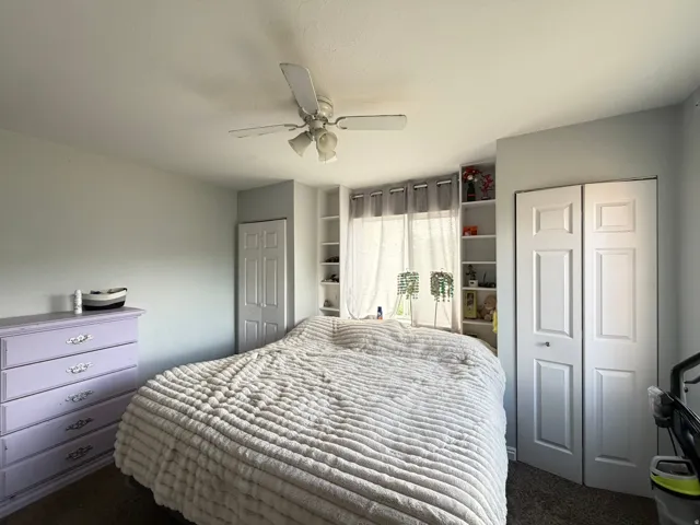 Bedroom featuring a ceiling fan with integrated lighting, built-in shelving, and bifold closet doors