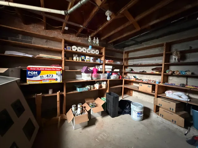 Expansive storage area featuring extensive built-in shelving, concrete flooring, exposed ceiling joists, and visible utility lines