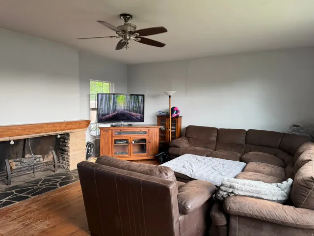 Living area featuring a stone fireplace with a wood mantle, hardwood flooring, and a ceiling fan