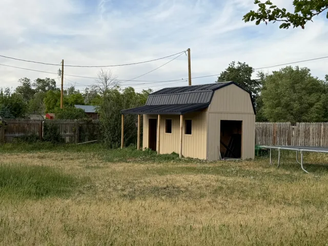 Cream-colored outbuilding with a black metal gambrel roof and an extended overhang