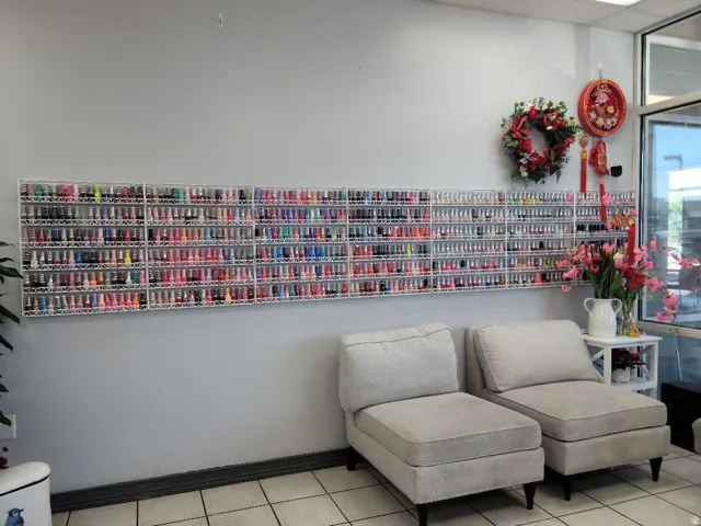 Wall-mounted shelving units displaying numerous small bottles, light gray wall, two upholstered lounge chairs with dark legs, and tiled flooring