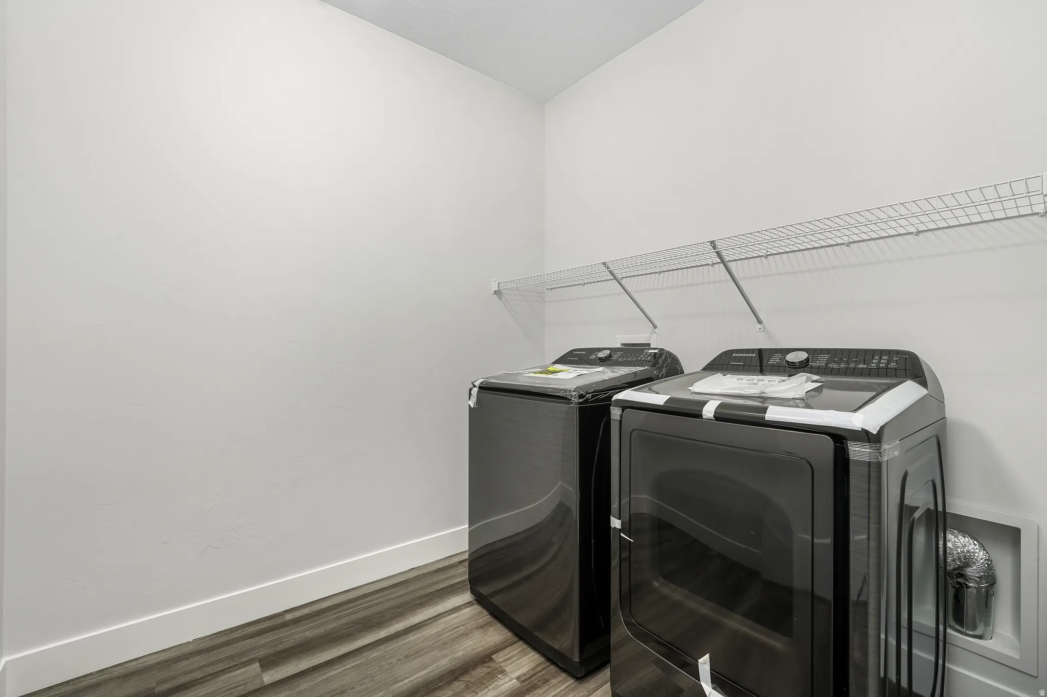 Dedicated laundry space featuring a wire shelf for storage, light-toned walls, and wood-finish flooring