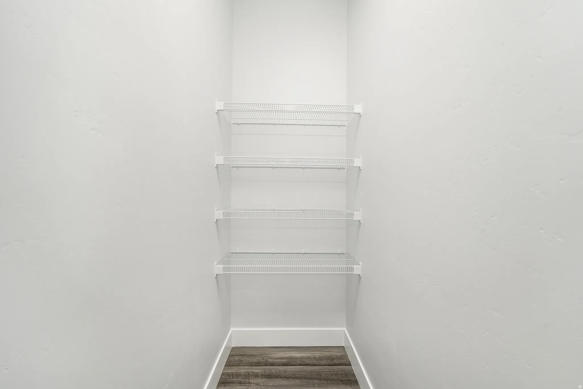 Built-in wire shelving system with four shelves, white painted walls, and wood-finish flooring