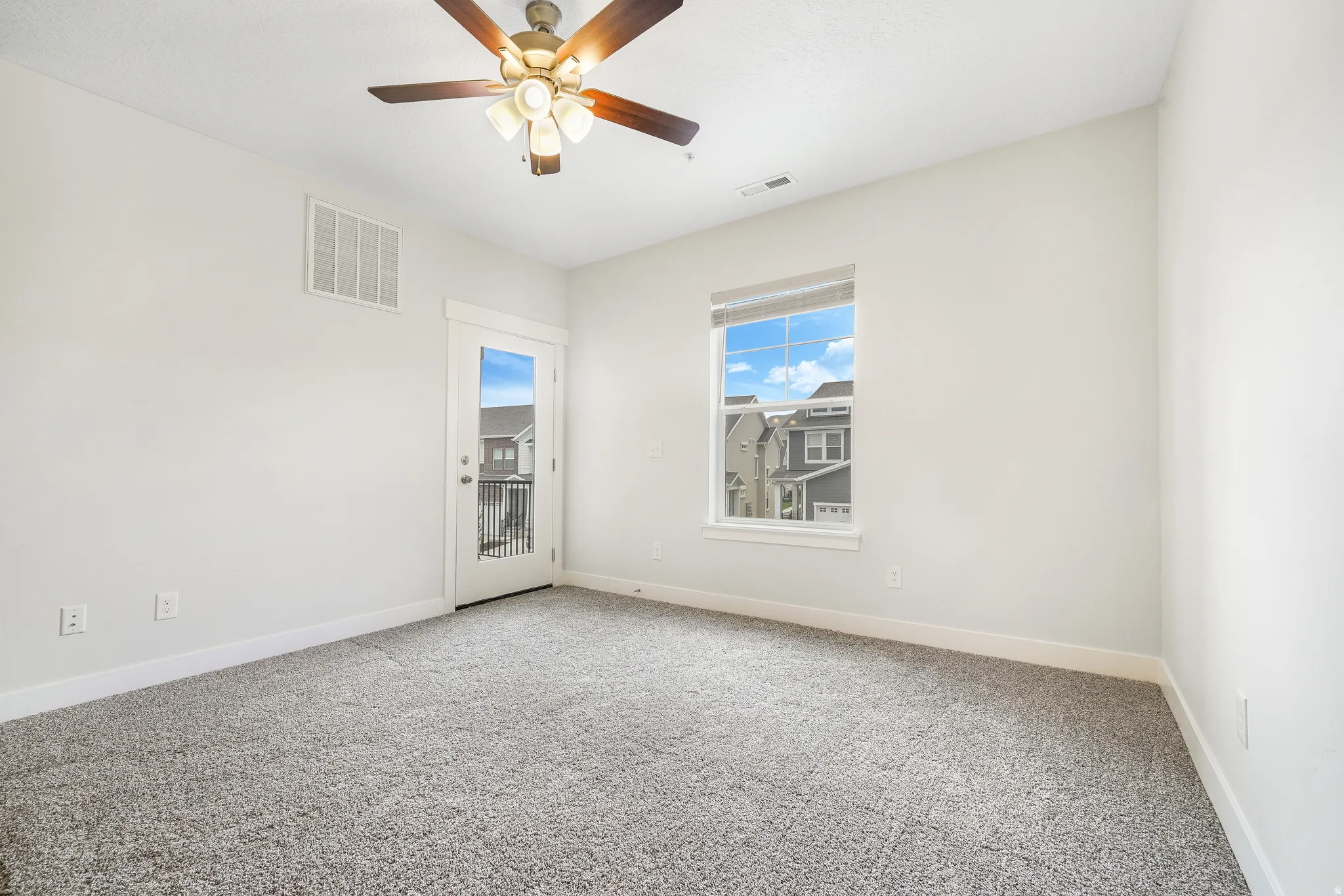 Bedroom featuring plush gray carpeting, a glass-paneled door opening to a private balcony with black railings, and a window providing natural illumination
