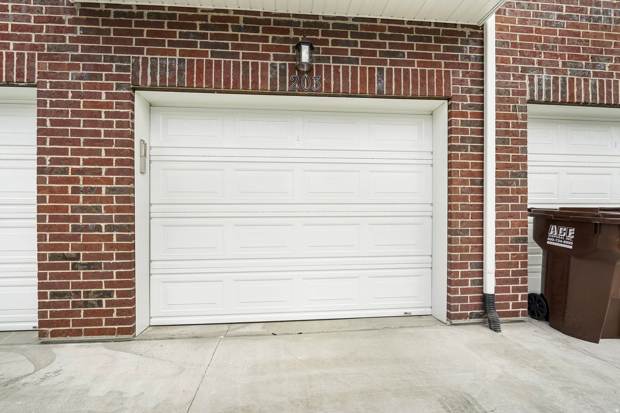Red brick exterior featuring a white paneled garage door with an overhead light fixture