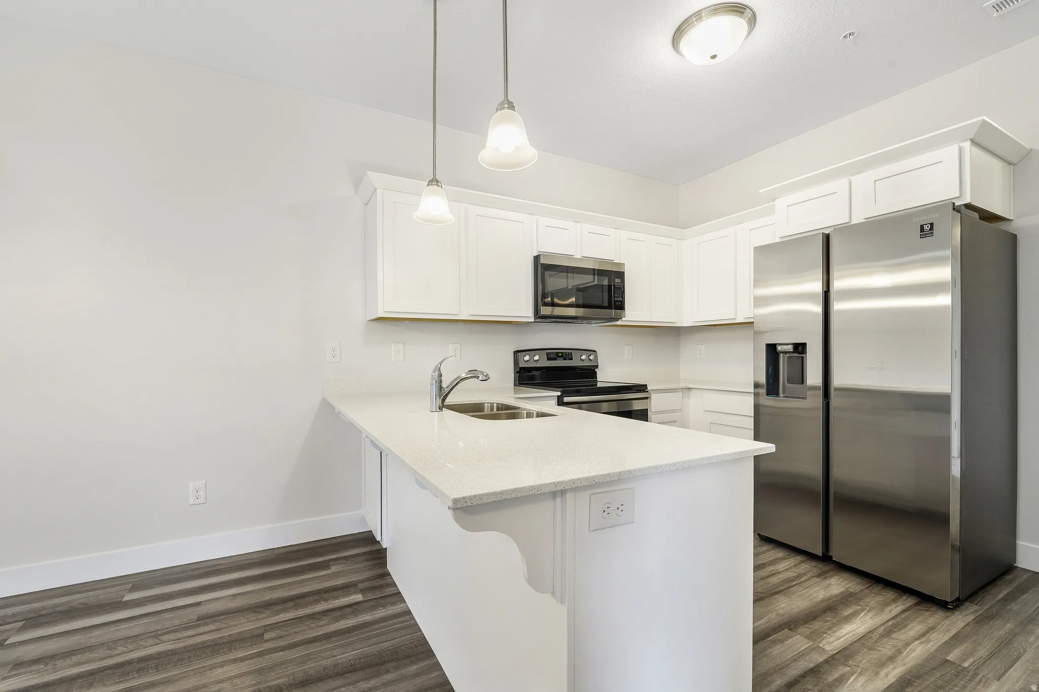 Kitchen featuring white cabinetry, light-toned countertops, stainless steel appliances, and wood-finish flooring