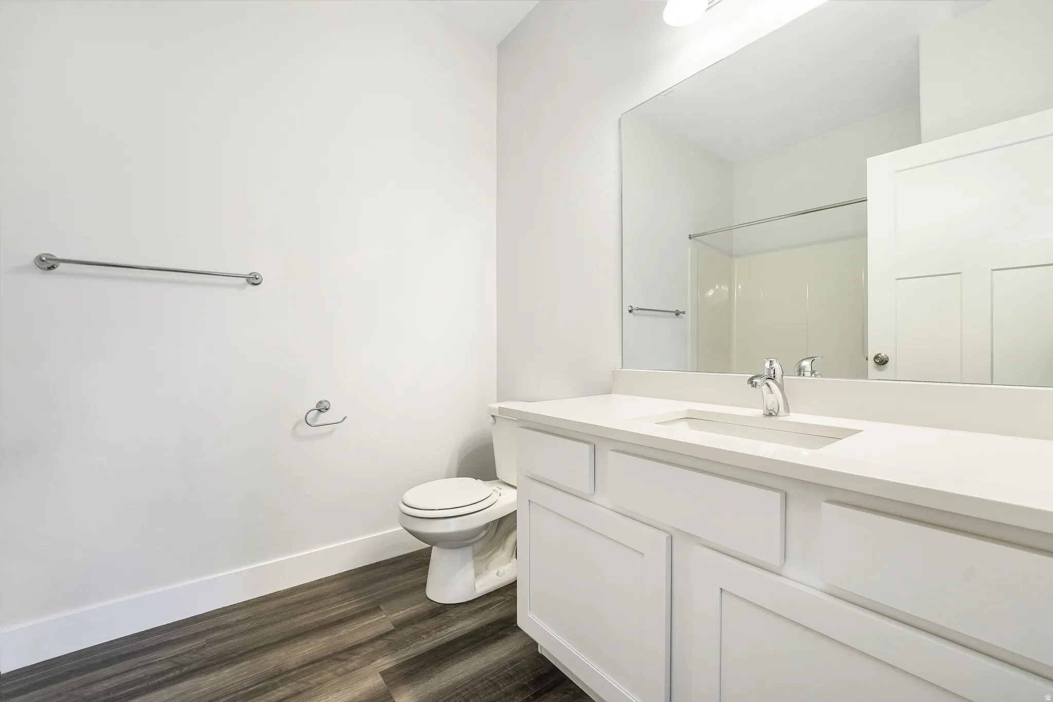 Full bathroom featuring a white vanity with integrated sink, a large mirror, chrome fixtures, wood-finish flooring, and a shower with clear enclosure