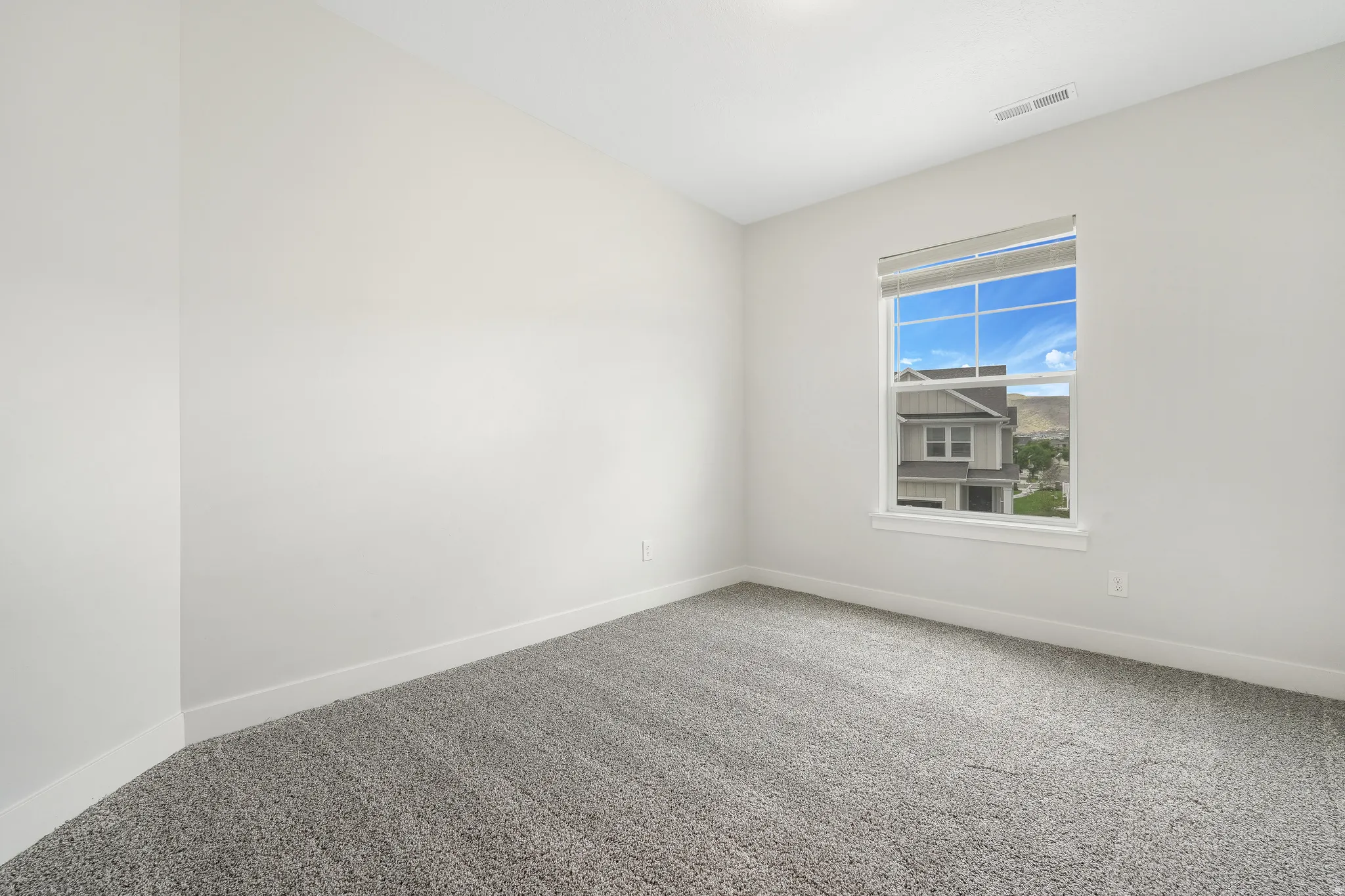 Room featuring a window with a roller shade, light gray carpeting, and white baseboards