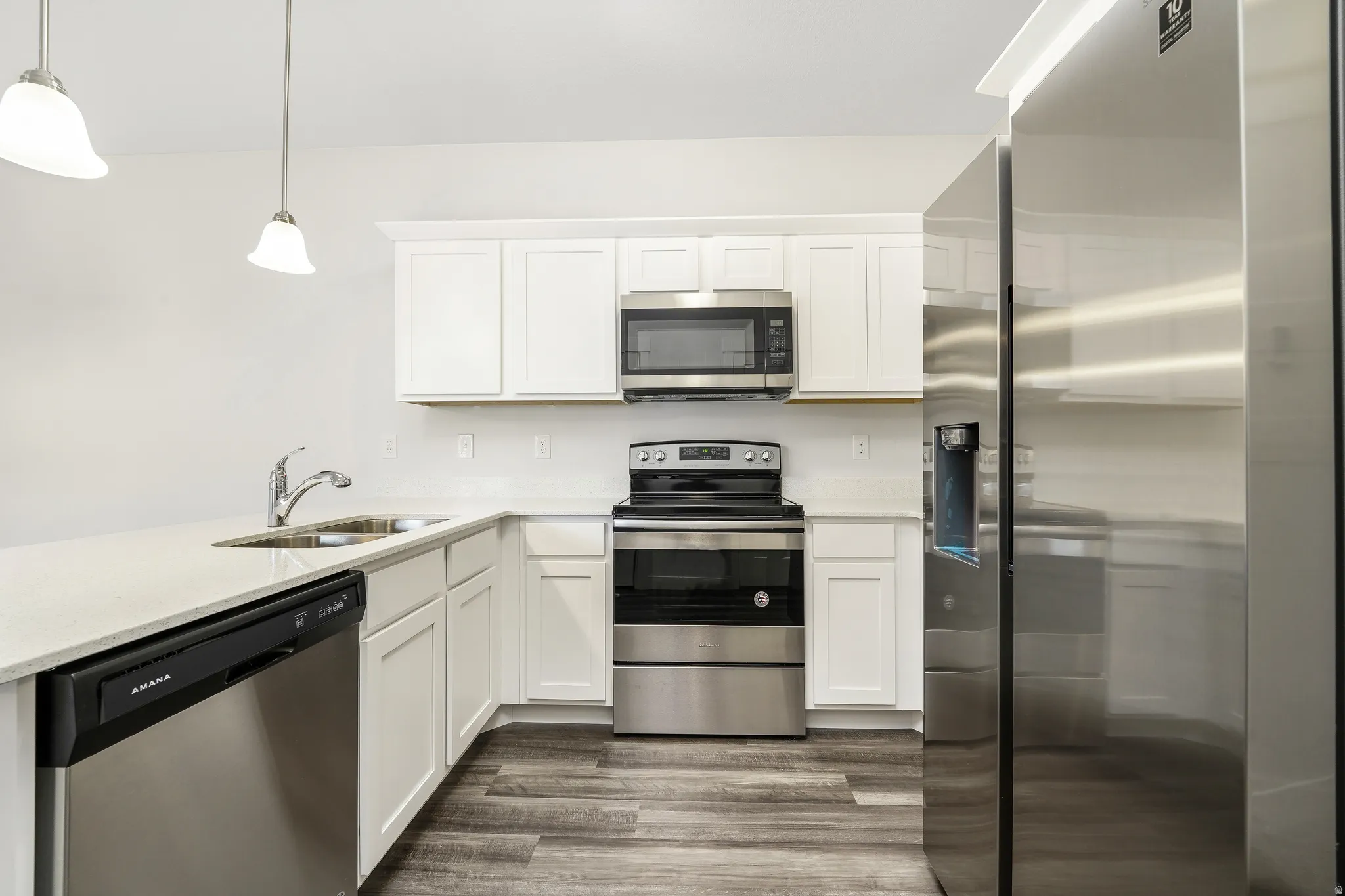 Modern kitchen featuring white shaker cabinetry, stainless steel appliances, quartz countertops, and wood-finish flooring