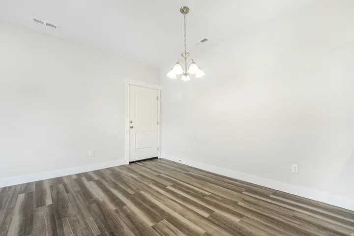 Spacious room featuring wood-finish flooring, white walls, and a multi-light chandelier