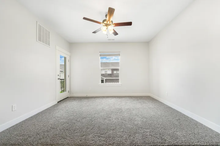 Spacious room featuring neutral carpeting, white baseboards, and a ceiling fan with integrated lighting