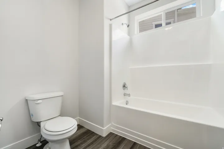 Full bathroom featuring a white tub/shower combination with chrome fixtures, a white toilet, and wood-finish flooring