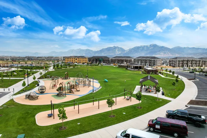 Expansive community park featuring a large green space, multi-structure playground, covered picnic areas, walking paths, and mountain scenery