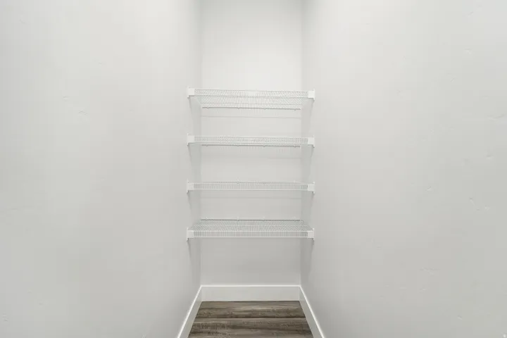 Built-in wire shelving system with four shelves, white painted walls, and wood-finish flooring