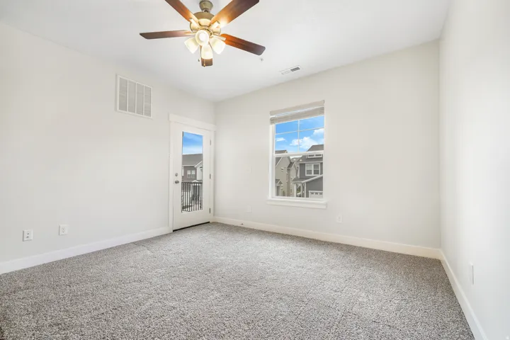 Bedroom featuring plush gray carpeting, a glass-paneled door opening to a private balcony with black railings, and a window providing natural illumination