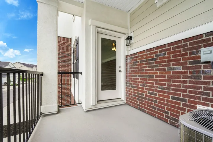 Outdoor patio featuring a glass-paneled door, black metal railings, textured stucco columns, brick detailing, and horizontal siding