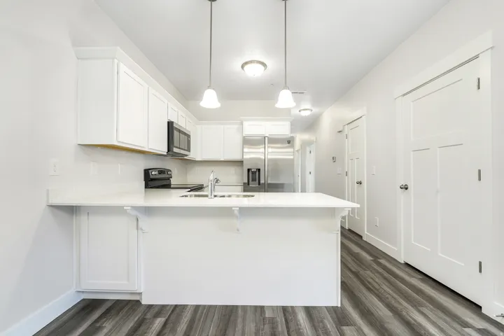 Modern kitchen featuring white cabinetry, light-toned countertops, stainless steel appliances, and wood-finish flooring