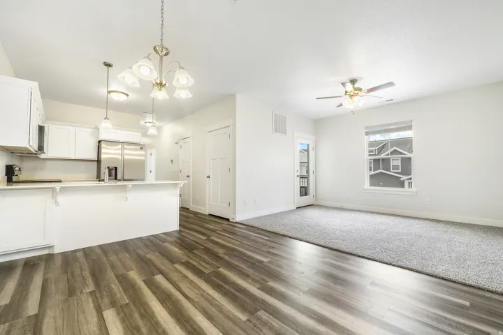 Open-concept living space featuring wood-finish flooring, a kitchen island with white cabinetry, stainless steel appliances, and ceiling fan