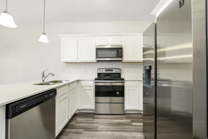 Modern kitchen featuring white shaker cabinetry, stainless steel appliances, quartz countertops, and wood-finish flooring