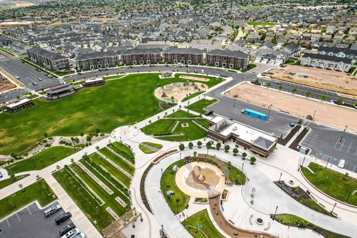 Expansive community park featuring a large green space, multiple play areas, paved pedestrian pathways, and a central water feature