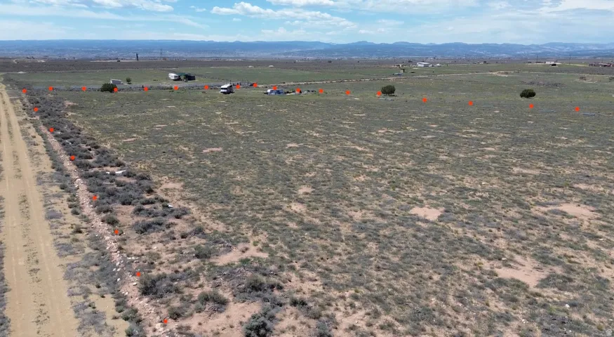 Expansive open land featuring a dirt road border, scattered natural vegetation, and distant mountain topography