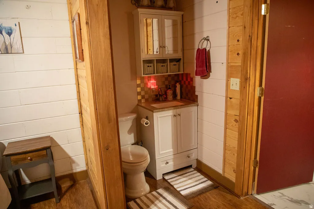 Compact bathroom featuring a white vanity with a brown countertop, a white toilet, and a tiled backsplash