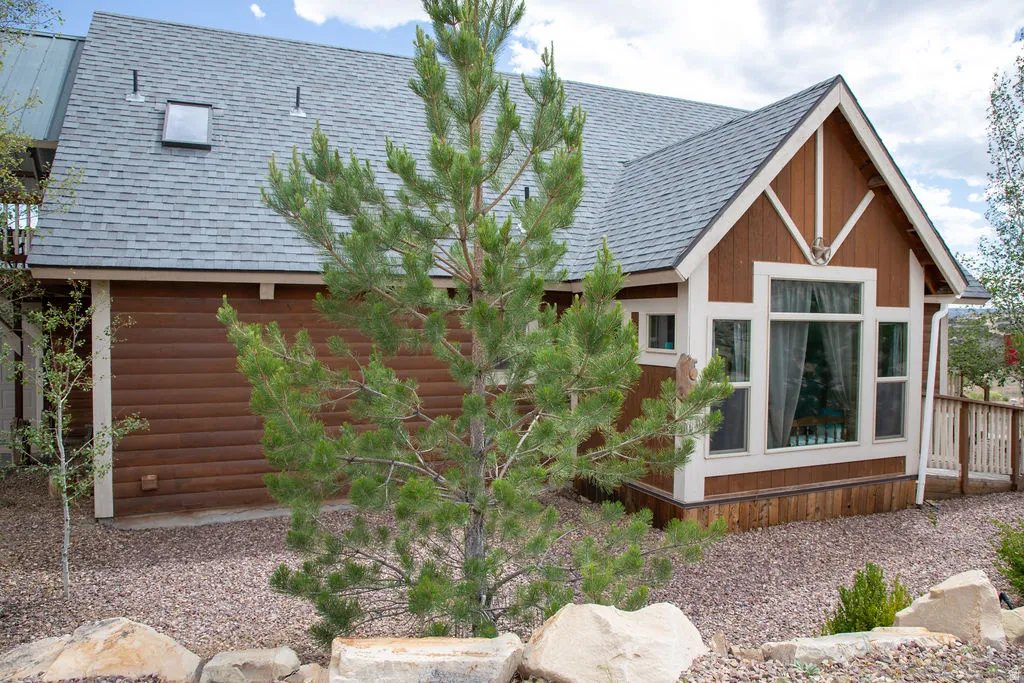 Exterior featuring log siding, an asphalt shingle roof with skylight, a prominent gable with decorative trim, and a window bay with multiple panes