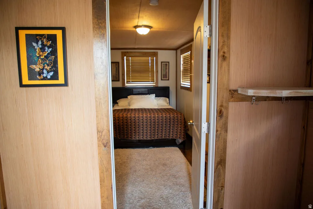 Bedroom space featuring wood-finish walls and doorframes, a ceiling-mounted light fixture, and horizontal window blinds
